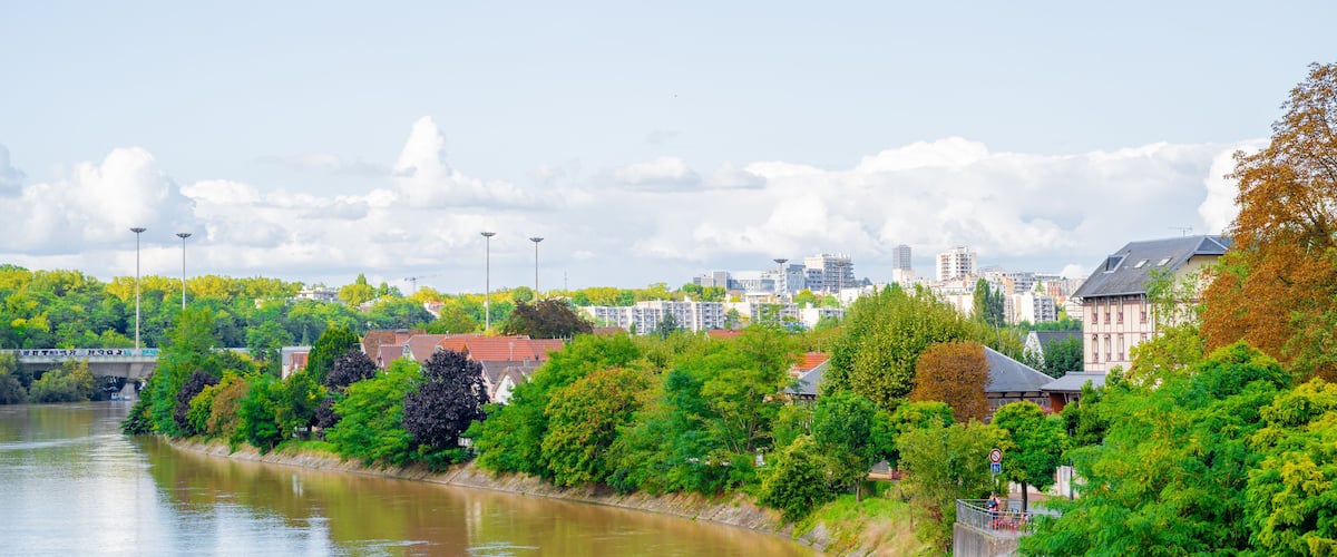 A river with a bridge, lush greenery, and buildings in the background.
