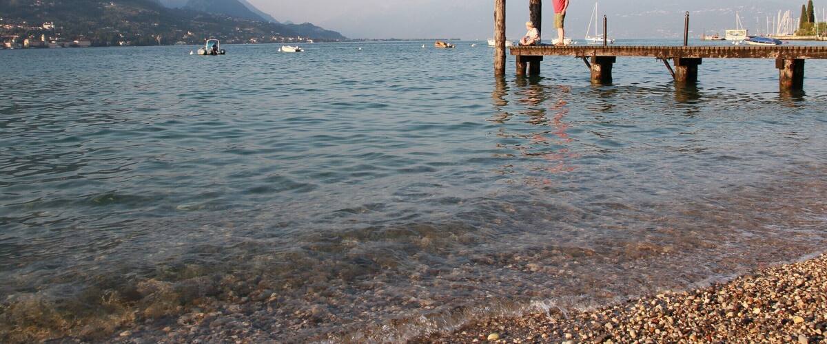 A pier extending into a calm lake with boats, mountains, and a clear sky.