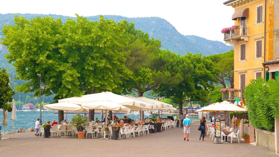 A lakeside outdoor dining area with tables and umbrellas, surrounded by trees and a mountain in the background.