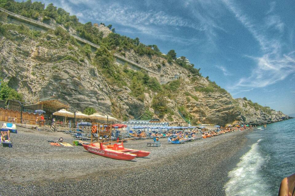 Una playa de guijarros con sombrillas y un bote rojo llamado SALVATAGGIO.