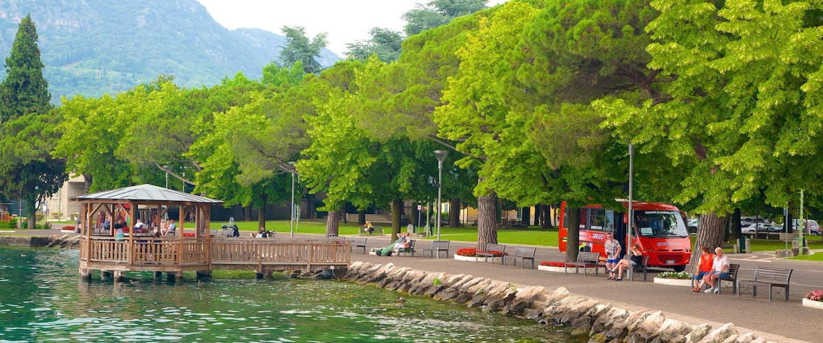 A lakeside park with a wooden gazebo, benches, and a red bus.