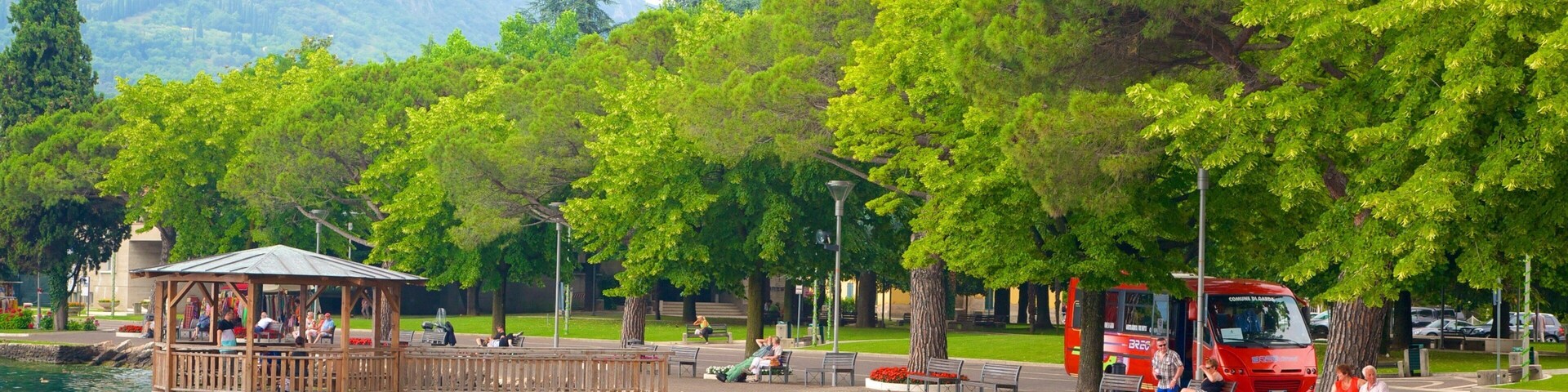 A lakeside park with a wooden gazebo, benches, and a red bus.