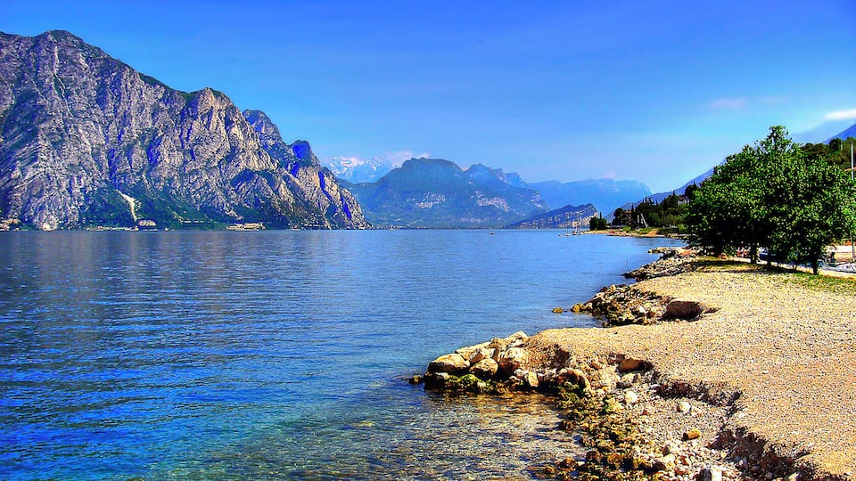 A clear lake with rocky shores and mountains in the background.