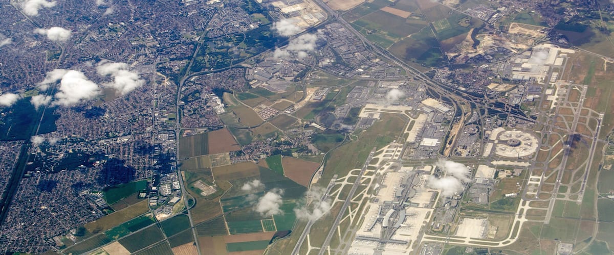 An aerial view of a city with a large airport, surrounding fields, and scattered clouds.