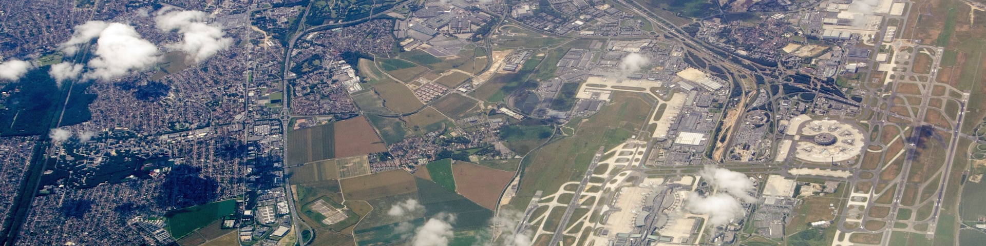 An aerial view of a city with a large airport, surrounding fields, and scattered clouds.