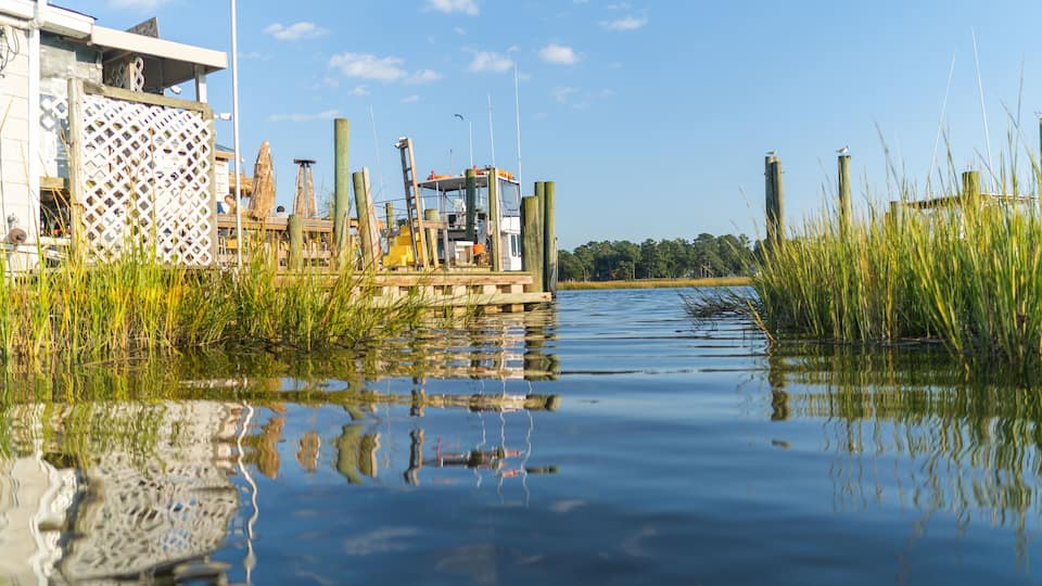 A calm waterway with a dock, wooden posts, and a building with a lattice facade.