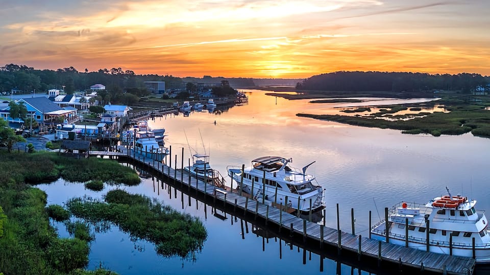 A river with a dock, boats, and a sunset.