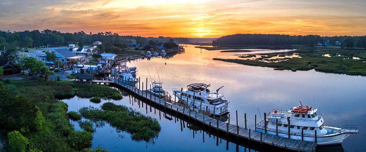 A river with a dock, boats, and a sunset.