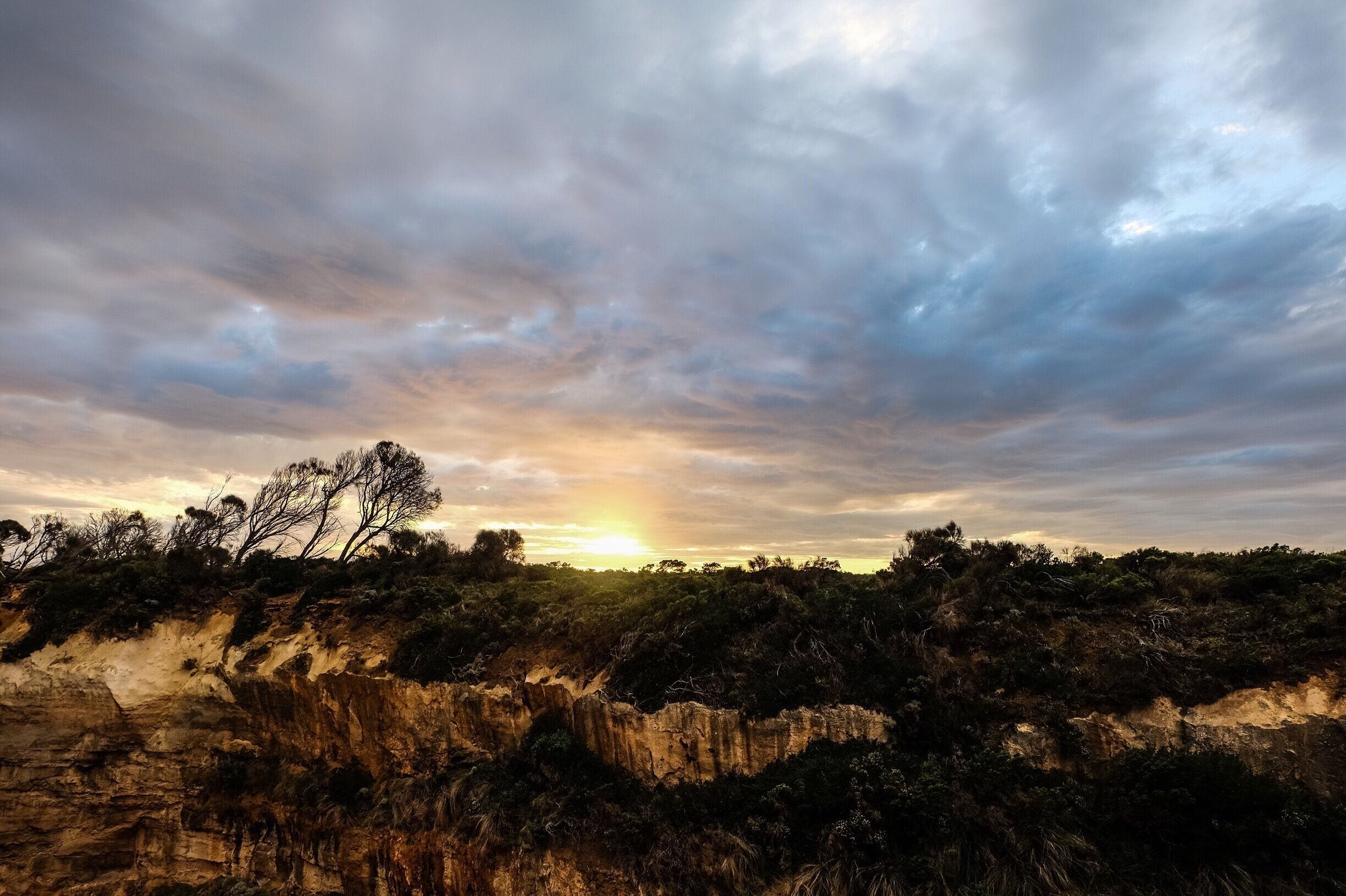 A sunset over a rugged landscape with sparse trees and cliffs.