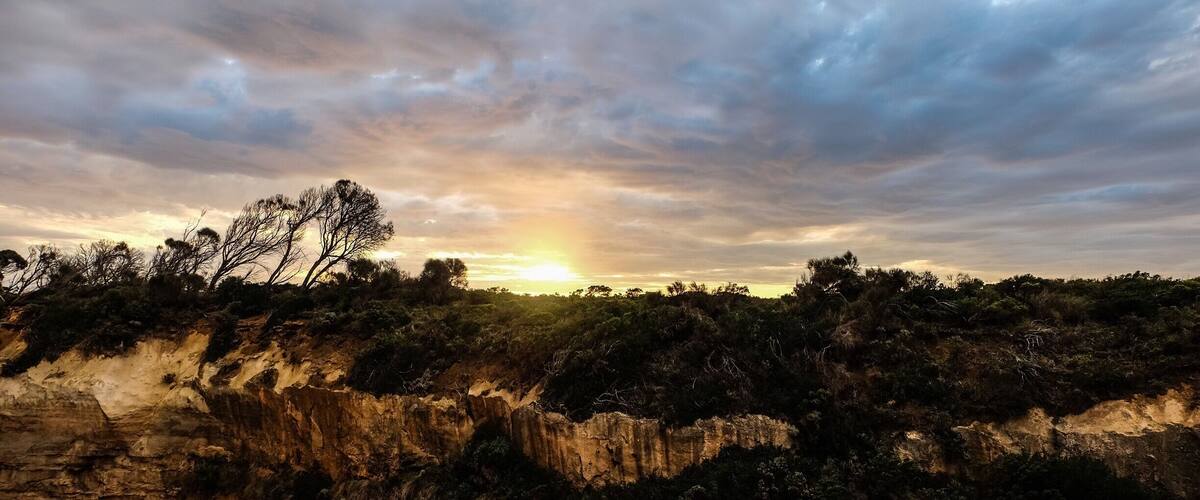 A sunset over a rugged landscape with sparse trees and cliffs.