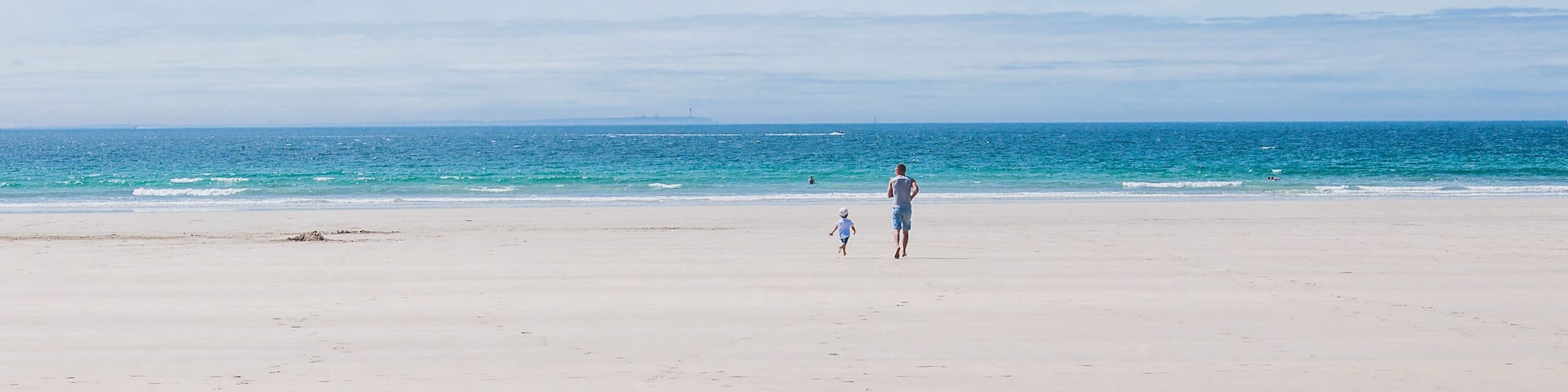 Father and son running towards the Atlantic Ocean on the beach in Finistere France