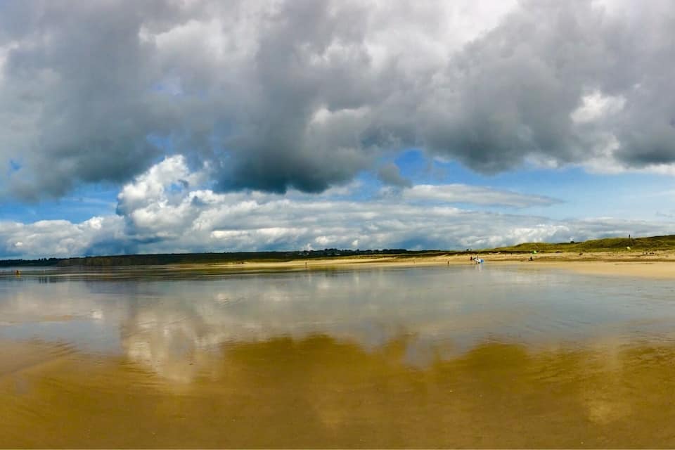 Ein Strand mit weiten, feuchten Sandflächen und bewölktem Himmel.