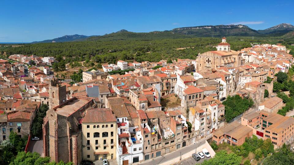 A densely built town with historic architecture, a prominent church, and mountains in the background.