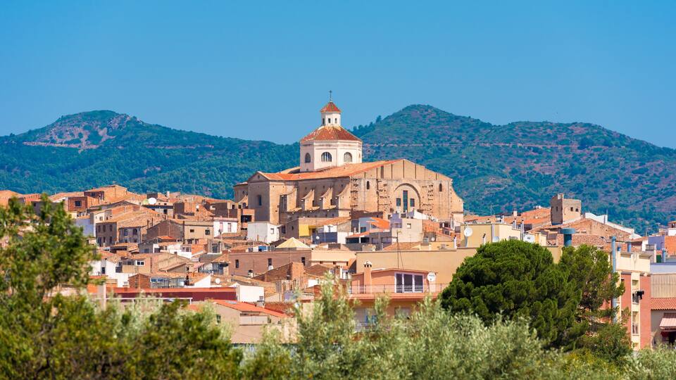 A historic town with a prominent church and surrounding buildings, set against a backdrop of green hills.