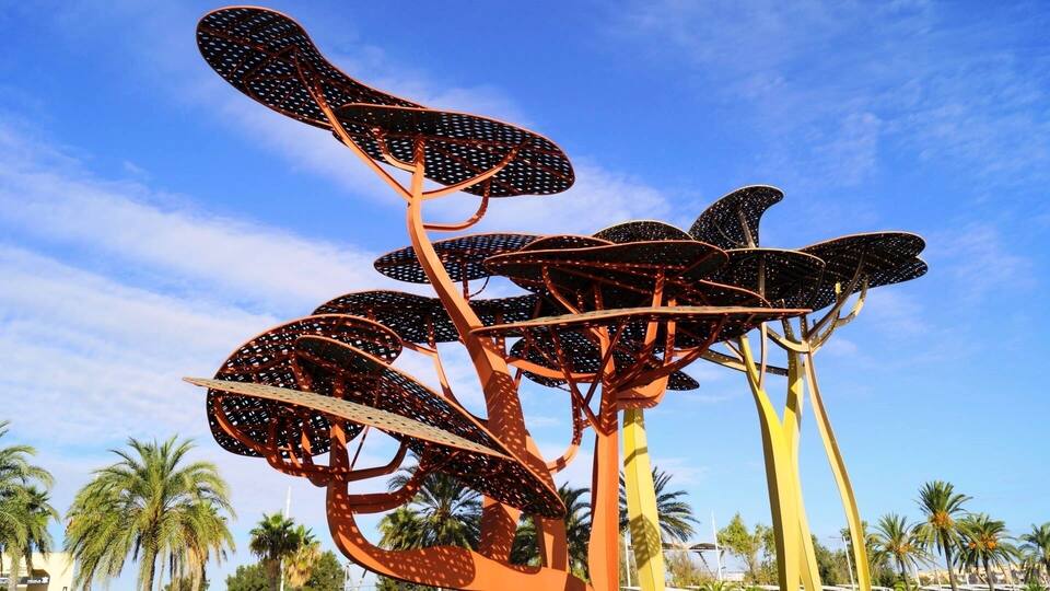 A large, abstract metal sculpture with multiple curved elements against a clear blue sky.