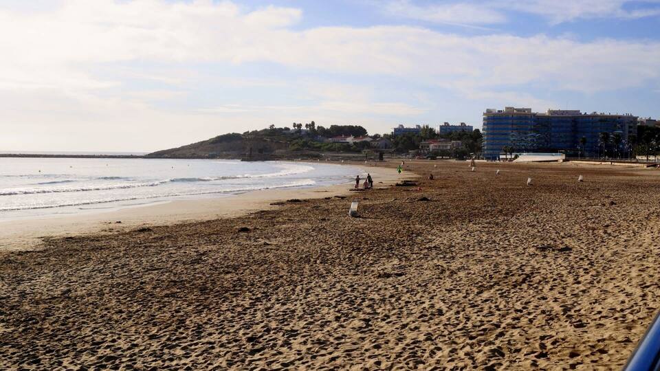 A beach with a rocky foreground, a sandy shore, and a building in the background.