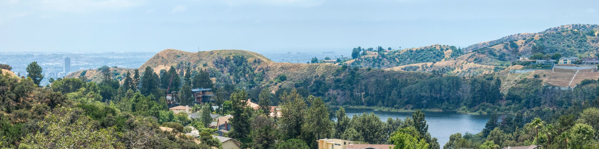 Un paisaje montañoso con un lago, casas y una silueta urbana distante.