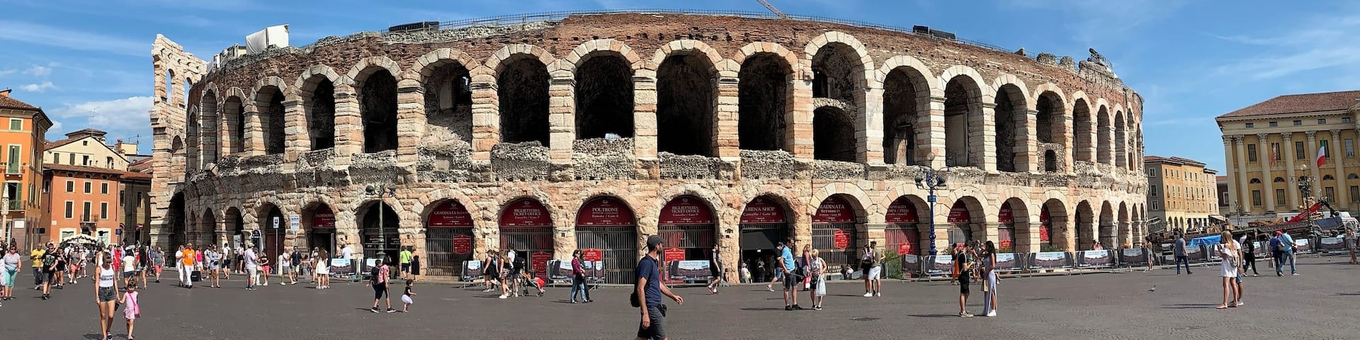 An ancient amphitheater with multiple arches and a crowd of people in the foreground.