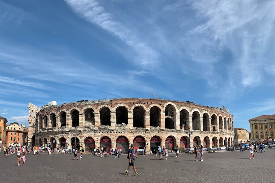 An ancient amphitheater with multiple arches and a crowd of people in the foreground.
