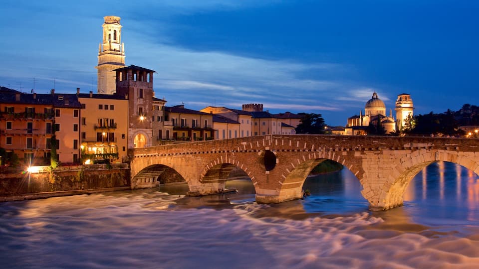 A stone bridge over a river with a tower and a dome in the background.