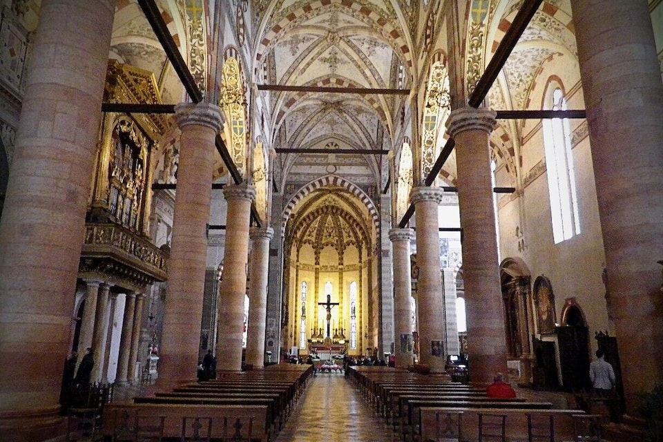 Interior de uma catedral com altos tetos abobadados, grandes colunas e um altar central.