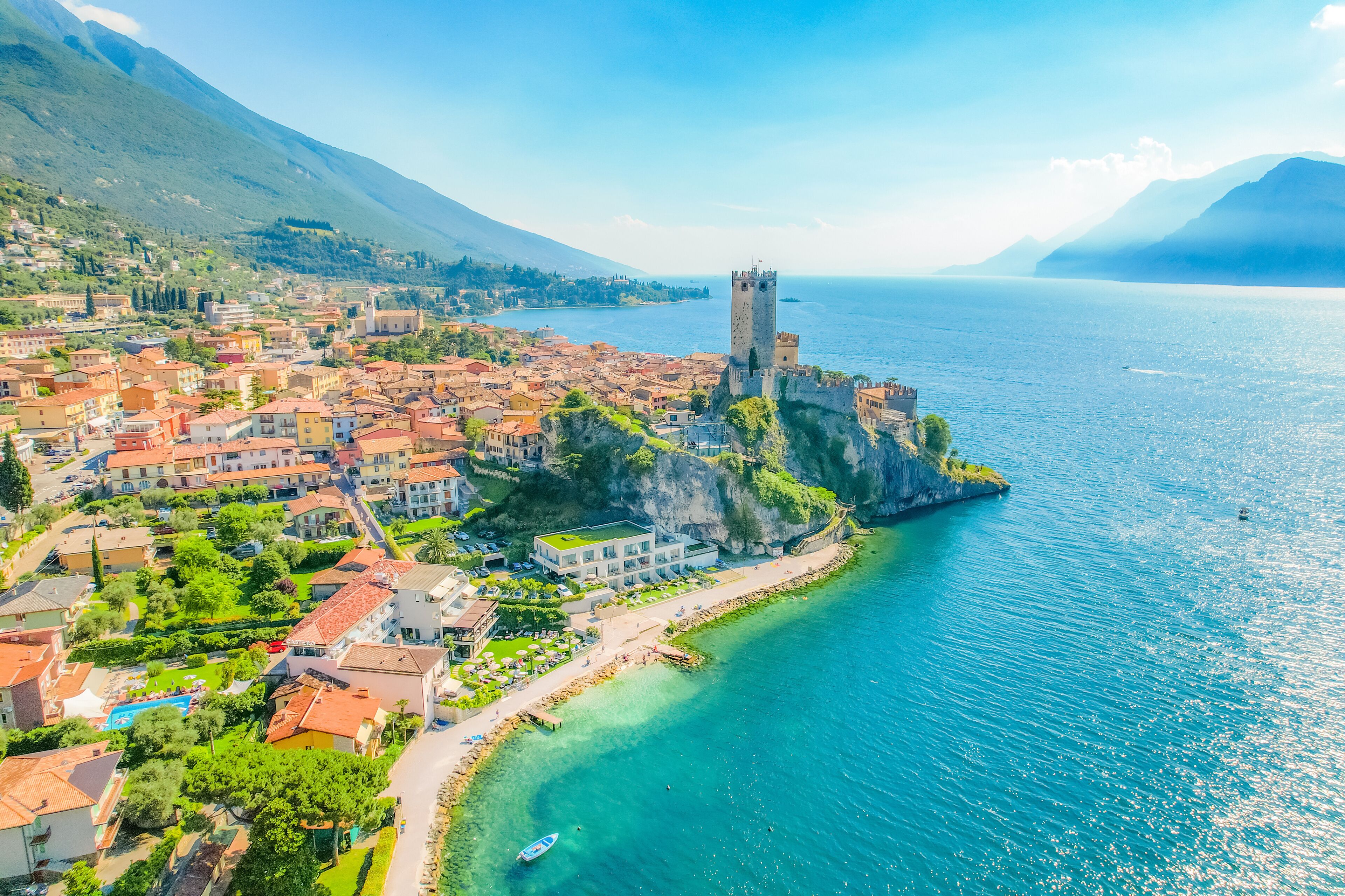 A coastal town with a prominent tower, clear blue waters, and a mountainous backdrop.