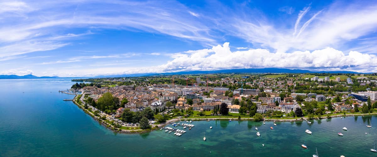 A panoramic view of a coastal city with a harbor, boats, and mountains in the background.