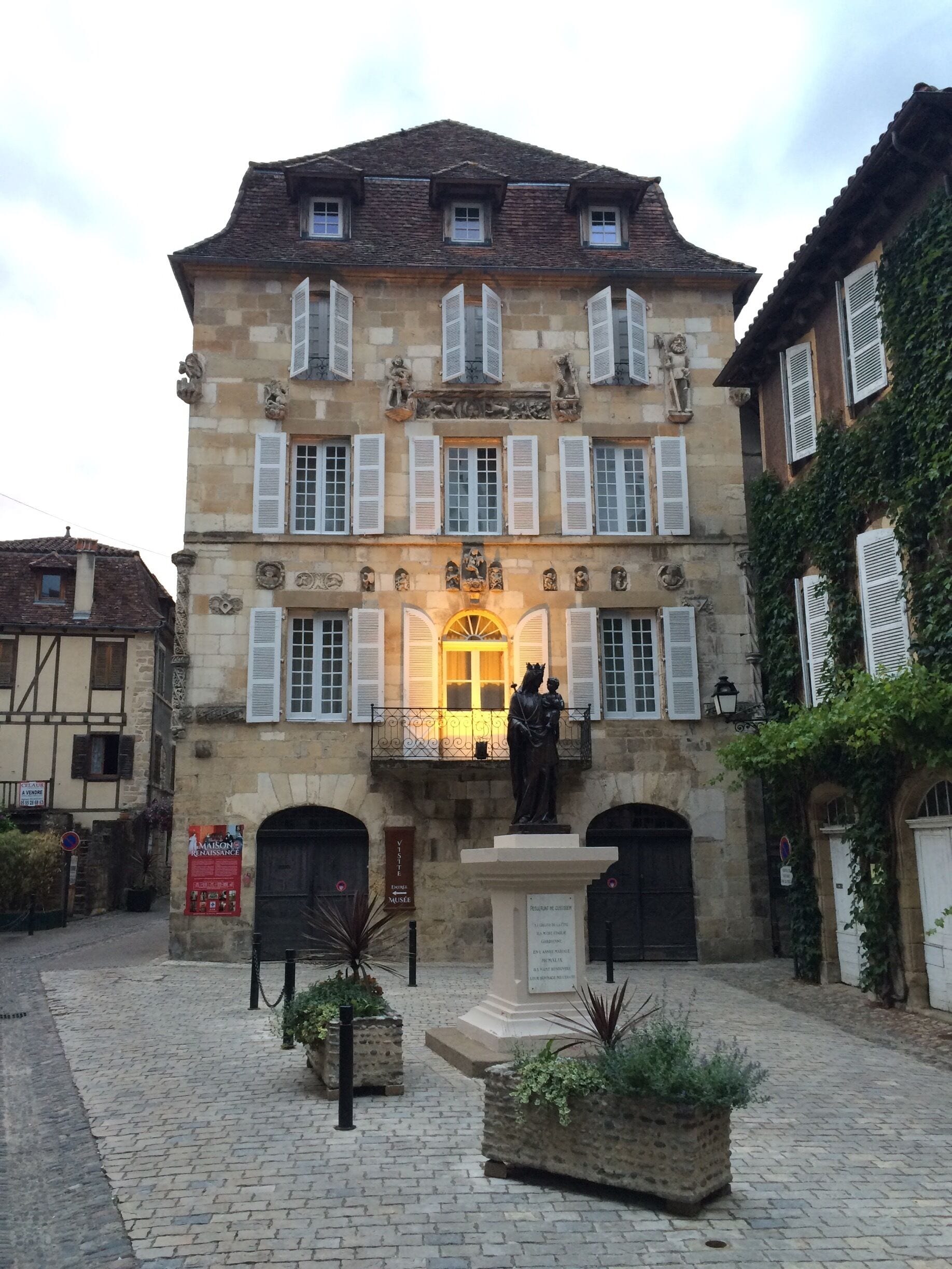 A historic building with a statue in front, stone walls, and a cobblestone courtyard.