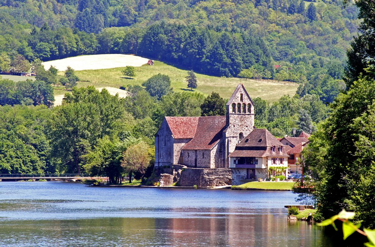 A historic church by a lake with a tower, surrounded by lush greenery and hills.