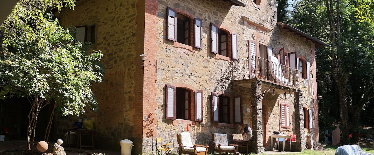 A stone building with a balcony, surrounded by trees and outdoor furniture.