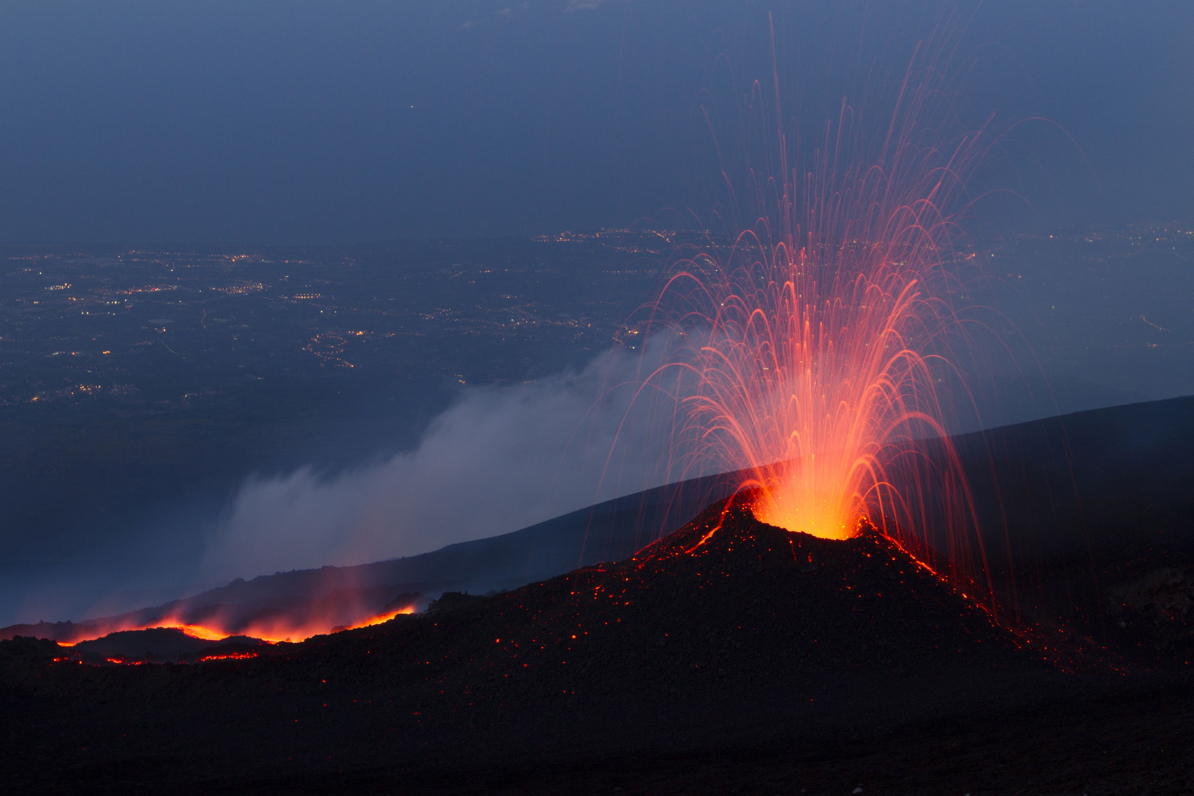 A volcano erupting at night with lava flowing down its side.