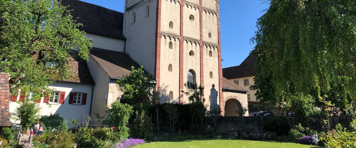 A historic church with a tall bell tower, surrounded by lush greenery and a well-maintained garden.