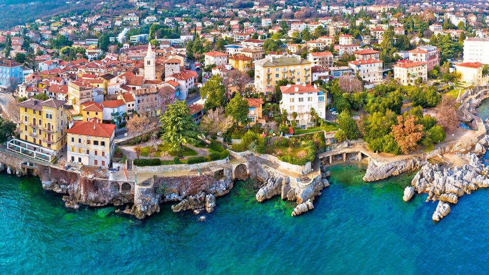 A coastal town with historic buildings, a rocky shoreline, and clear blue waters.