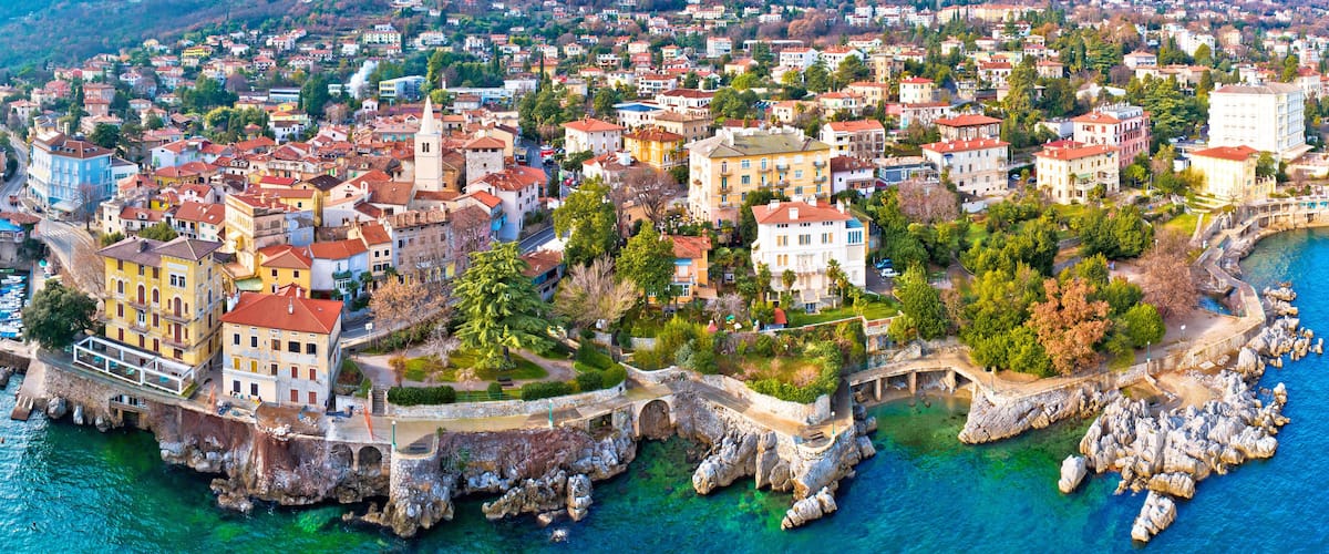 A coastal town with historic buildings, a rocky shoreline, and clear blue waters.