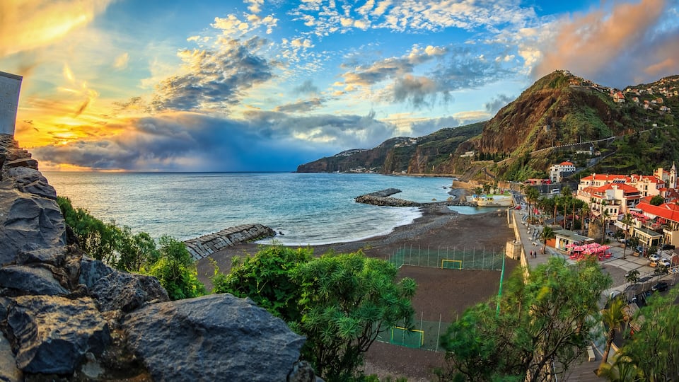 A coastal town with a beach, rocky cliffs, and houses with red roofs.