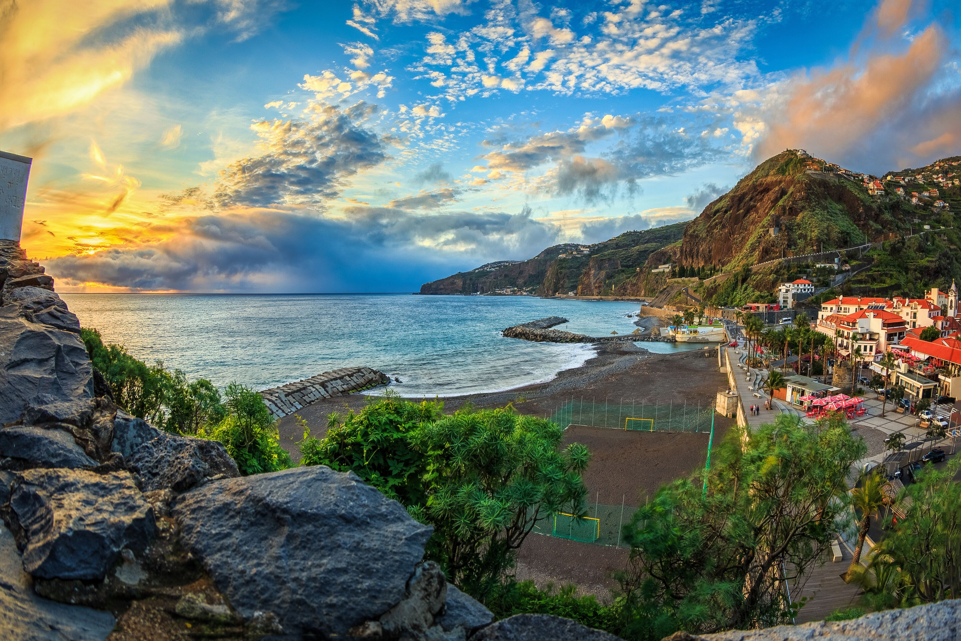 A coastal town with a beach, rocky cliffs, and houses with red roofs.