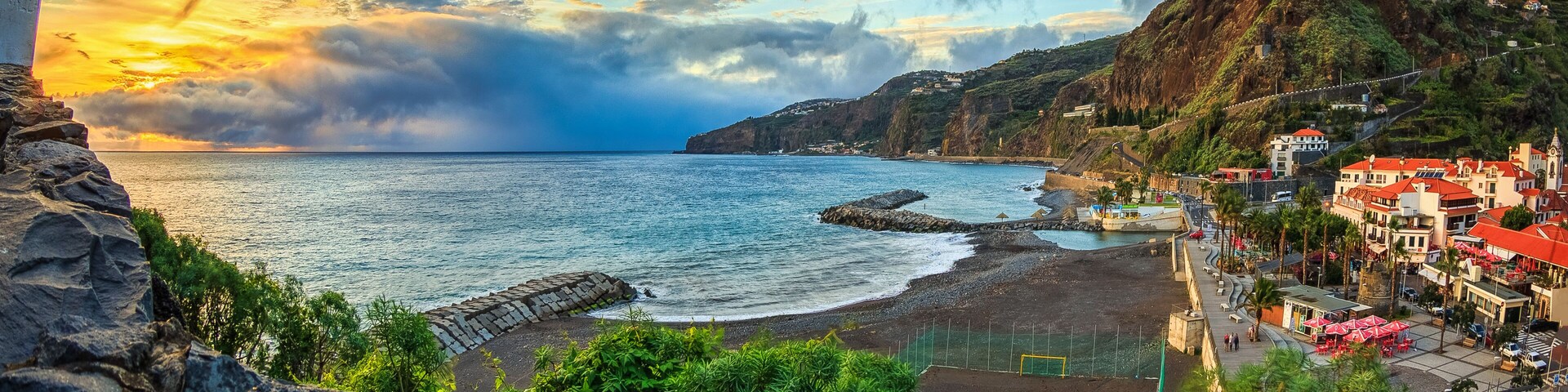 A coastal town with a beach, rocky cliffs, and houses with red roofs.