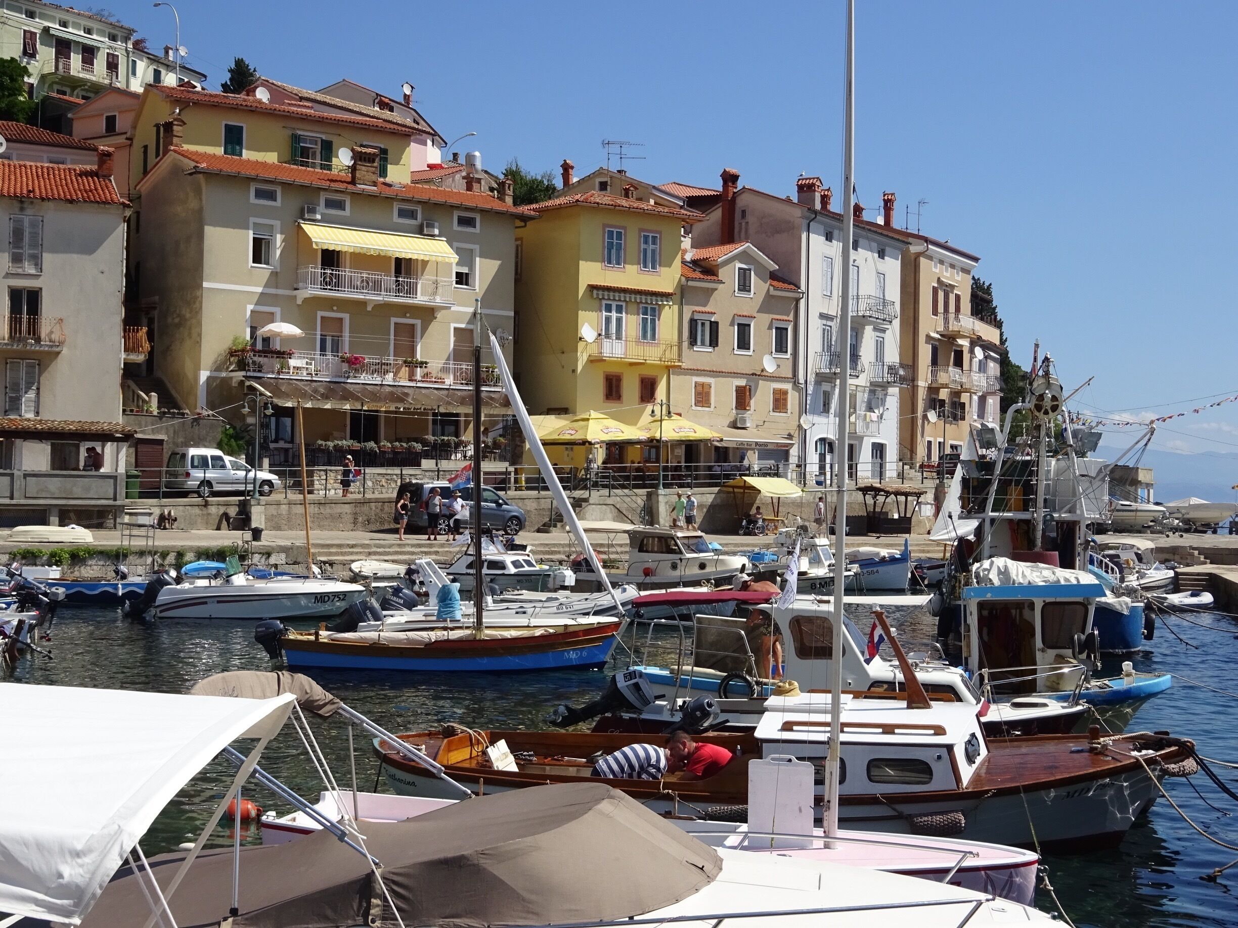 A marina with various boats docked, surrounded by colorful buildings and a clear blue sky.