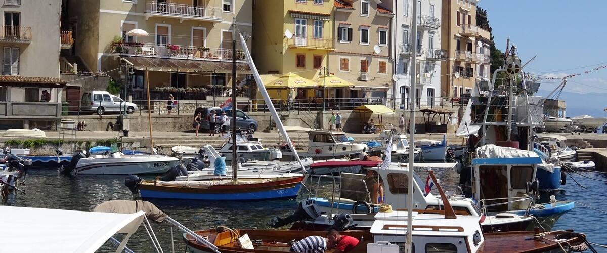 A marina with various boats docked, surrounded by colorful buildings and a clear blue sky.