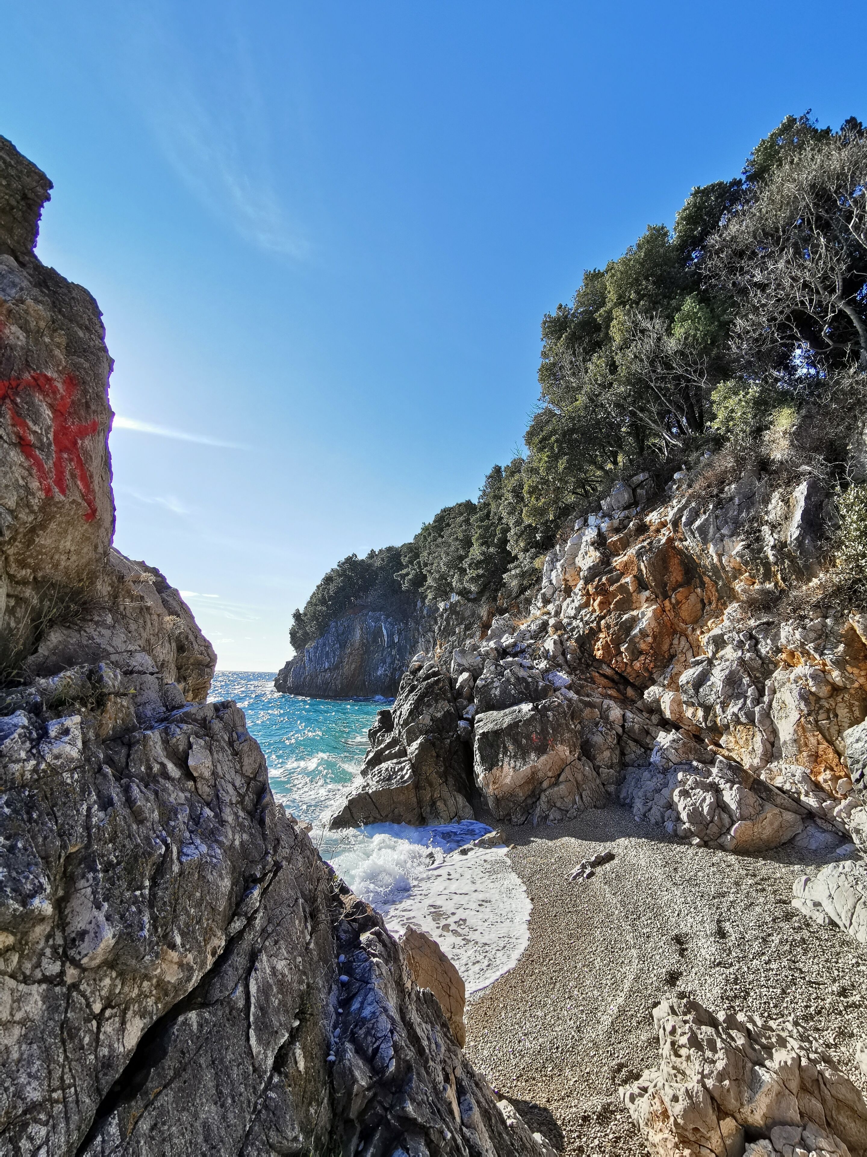 A rocky coastline with clear blue waters and a sandy beach.