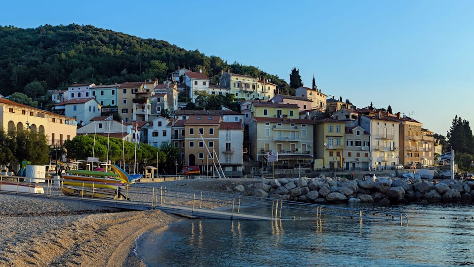 A coastal town with buildings, a rocky beach, and fishing boats.