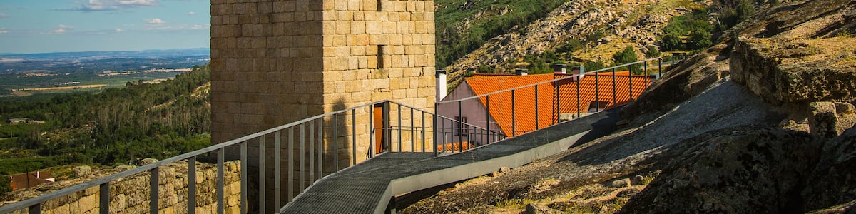 A stone tower with a cross on top, a red-roofed building, and a hilly landscape.