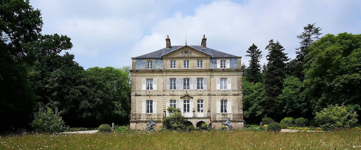 A large, historic building with a symmetrical facade, surrounded by a lush garden and a field of wildflowers.