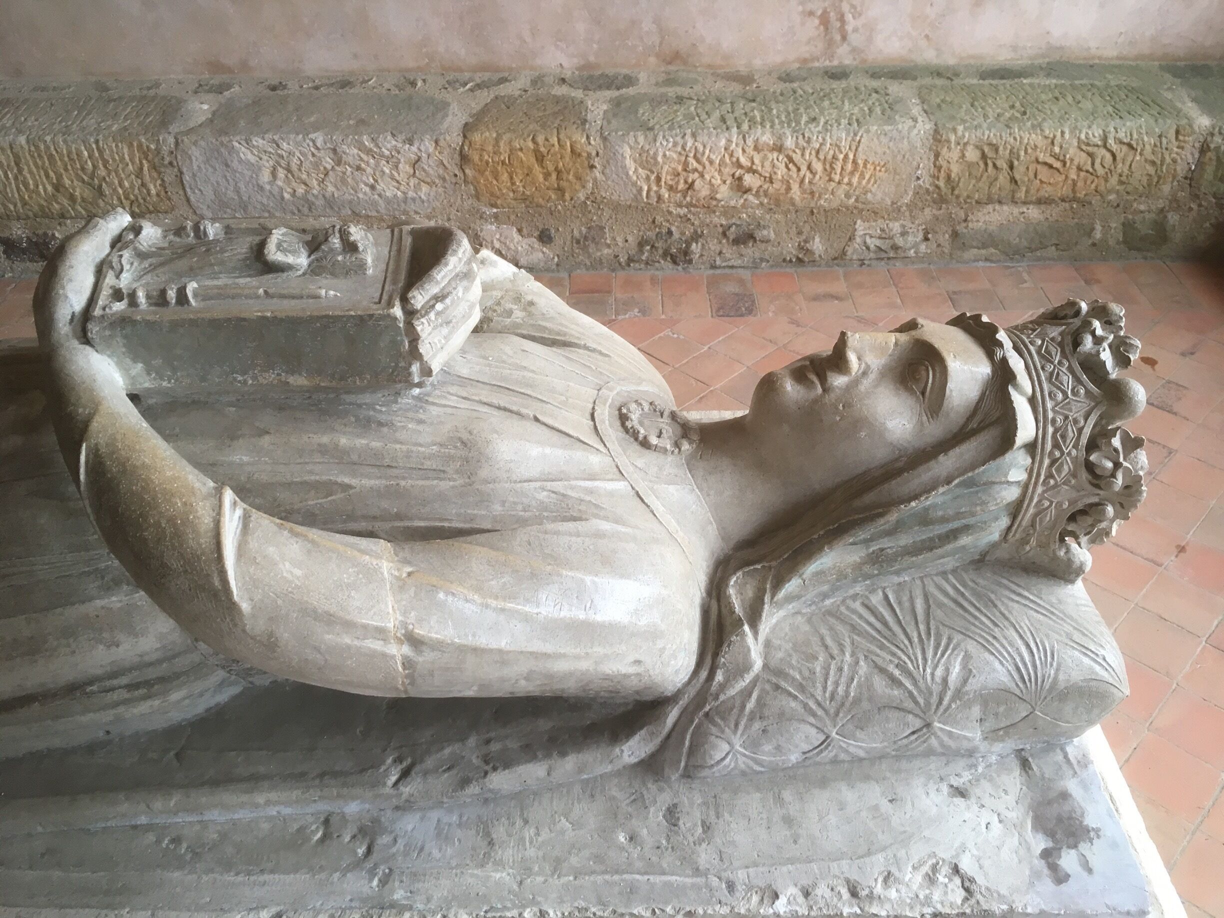 A stone sarcophagus with a reclining figure, intricate carvings, and a floral pattern on the pillow.