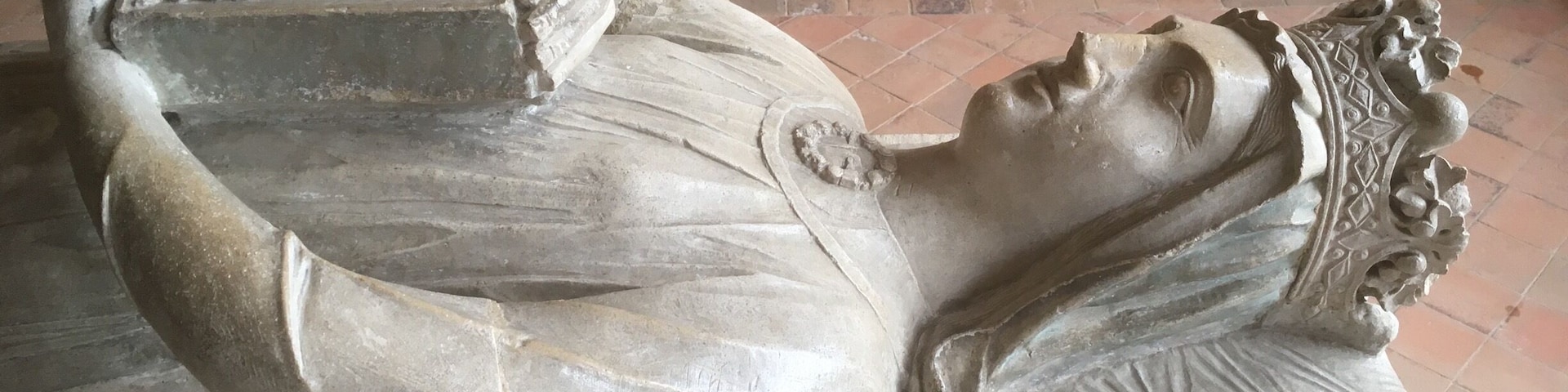 A stone sarcophagus with a reclining figure, intricate carvings, and a floral pattern on the pillow.