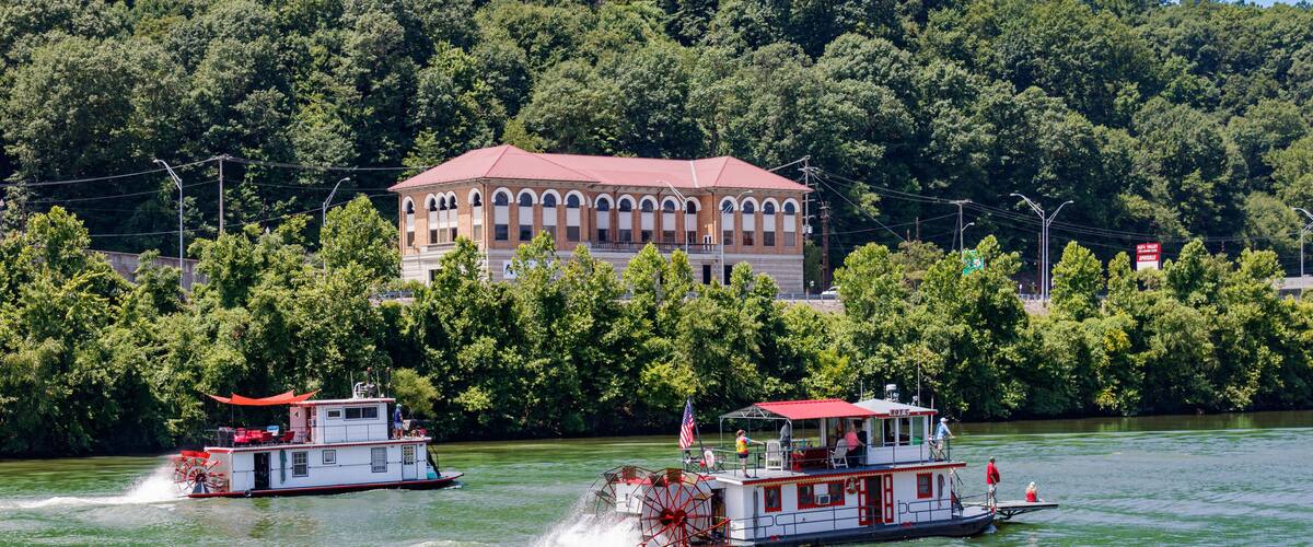 Two paddle boats on a river with a building in the background.