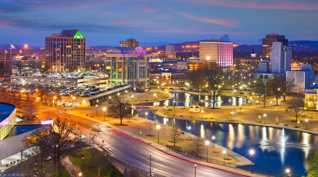 A cityscape at dusk with illuminated buildings, a river, and a bridge.
