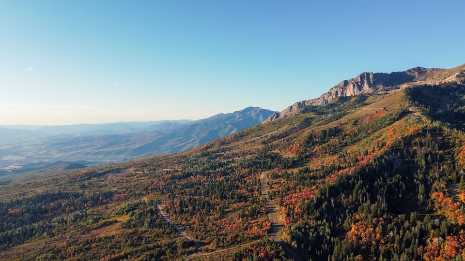 A mountainous landscape with autumn foliage, a winding road, and distant mountain ranges.