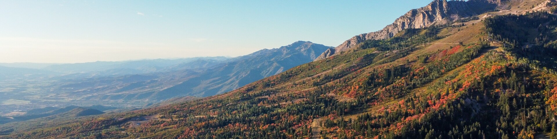 A mountainous landscape with autumn foliage, a winding road, and distant mountain ranges.