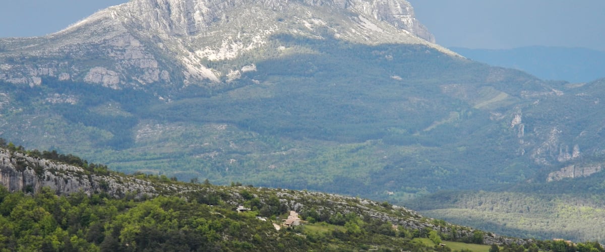 A mountain with a peak, forested slopes, and a small building in the foreground.